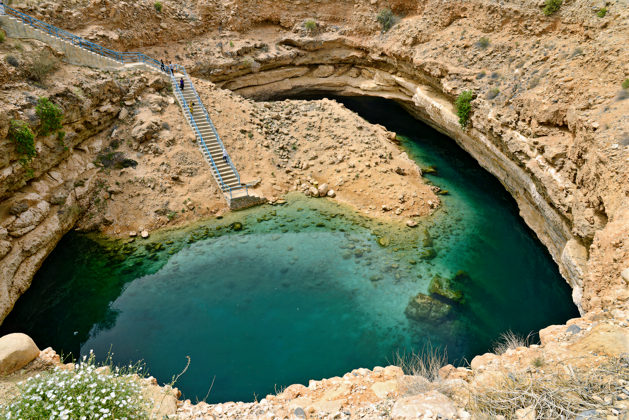 Crystal-clear turquoise waters of Bimmah Sinkhole, surrounded by rocky cliffs and lush greenery.