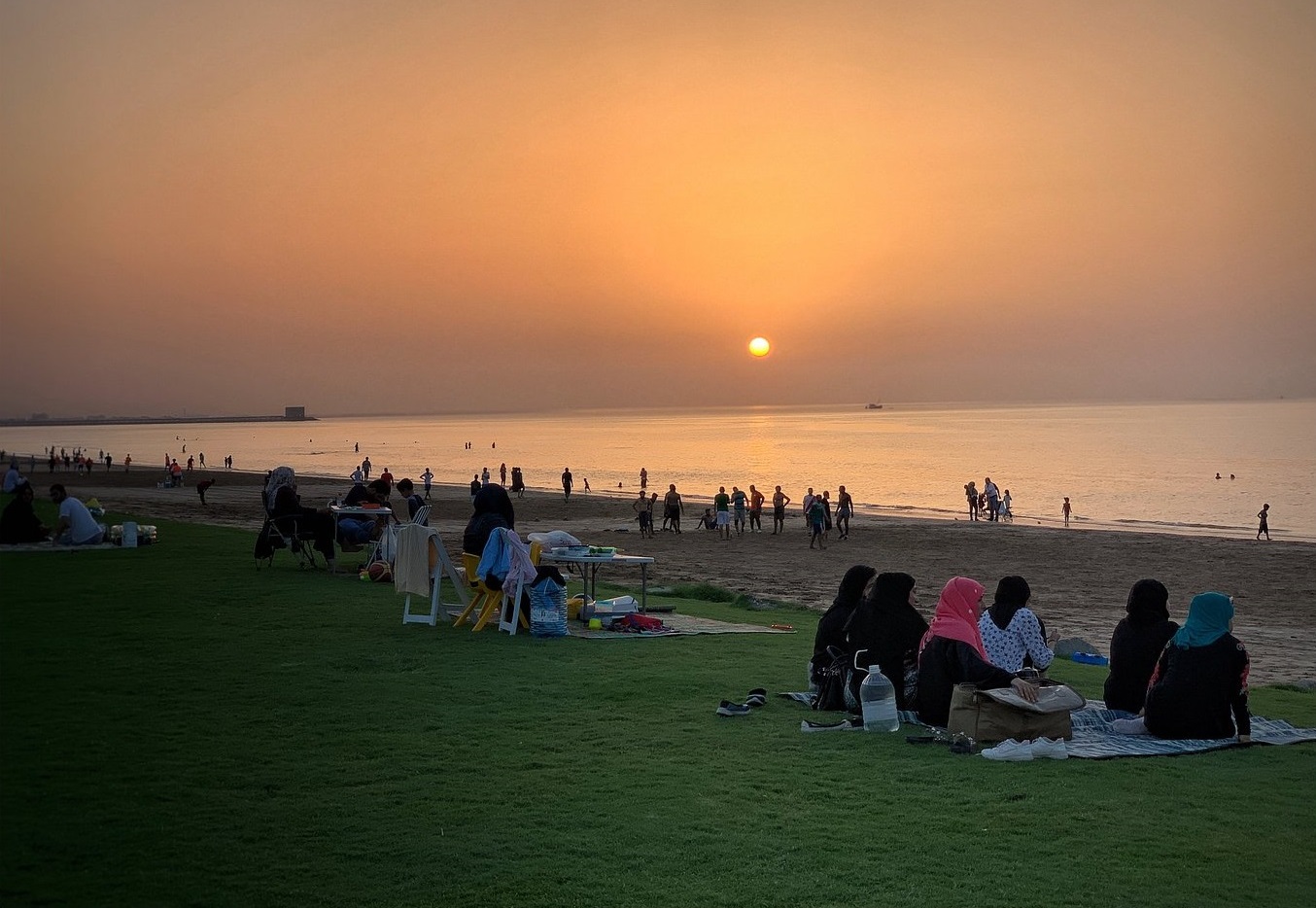 A breathtaking view of the serene Qurum Beach in Oman, with the golden sun setting on the horizon, painting the sky with hues of red and orange.